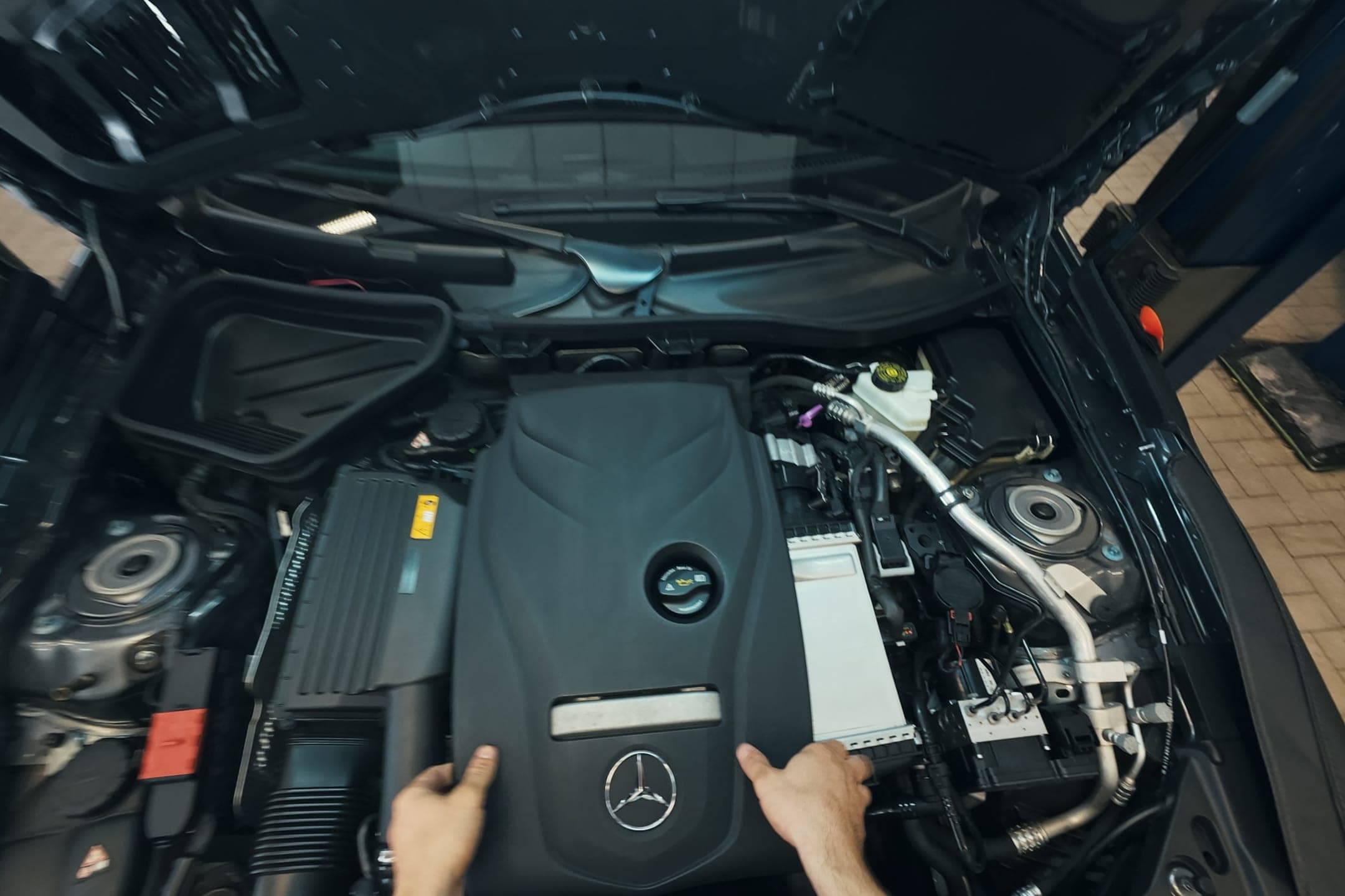 Le mani di un tecnico sul copri-motore di una Mercedes-Benz, col cofano aperto